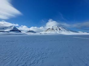image of a snow covered mountain in the distance, with snow in the foregound and blue sky